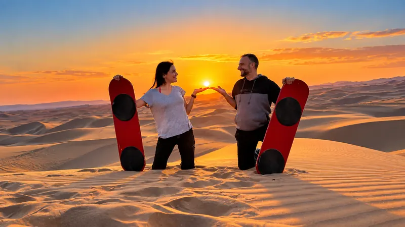 Pareja con tablas de sandboard en las dunas al atardecer