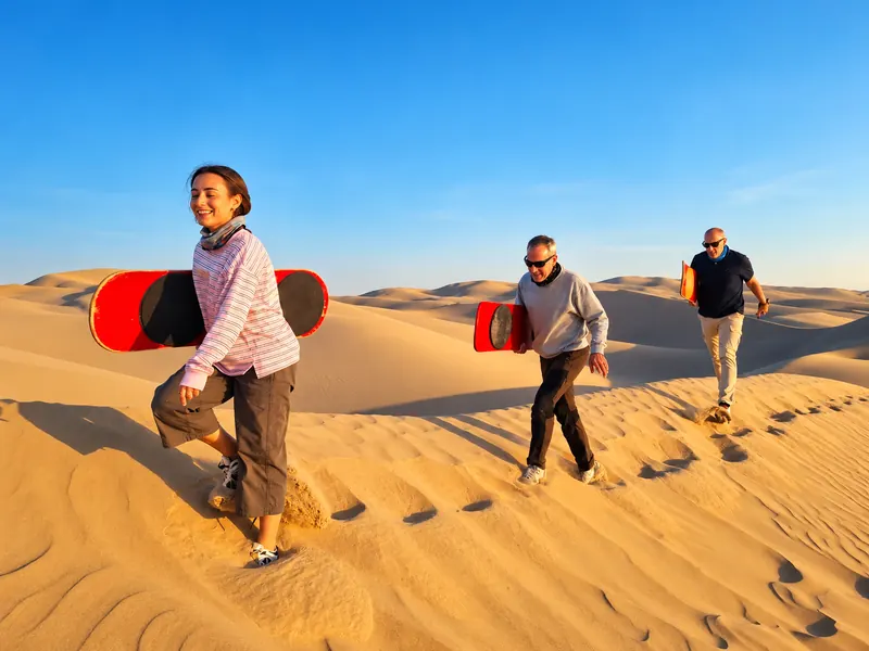 Viajera con tabla de sandboard en una duna dorada