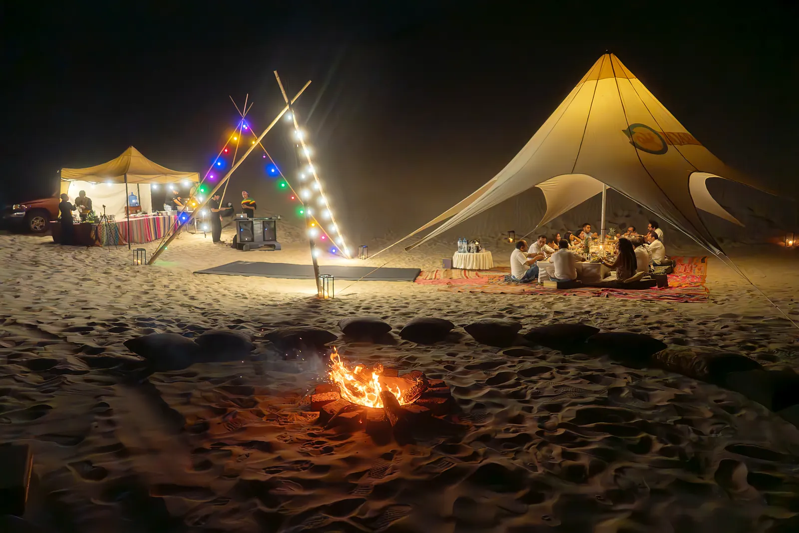 Campamento de la cena con fogata, faroles y toldo iluminado de noche en el Desierto California