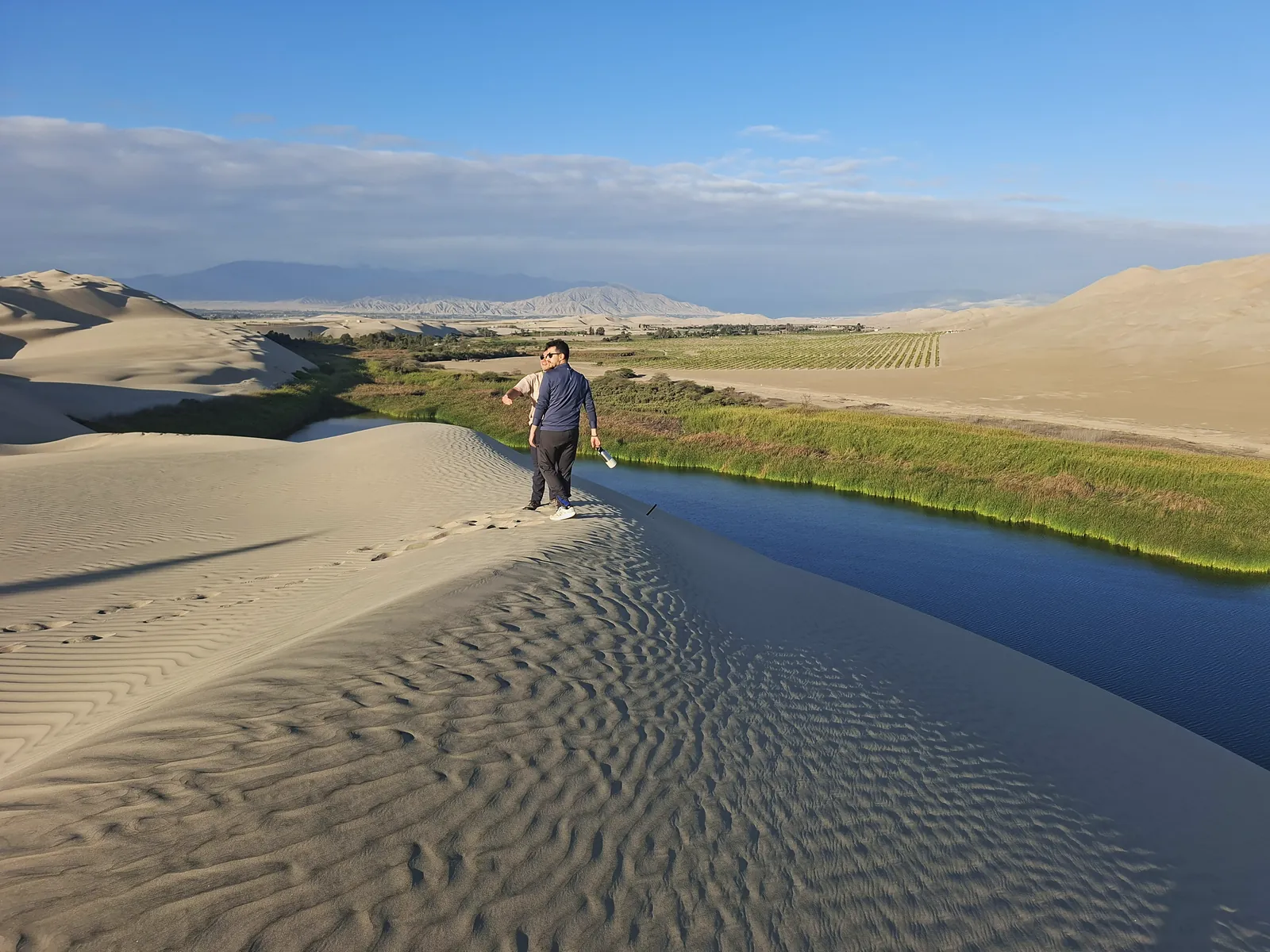Caminante en la cresta de una duna junto al oasis